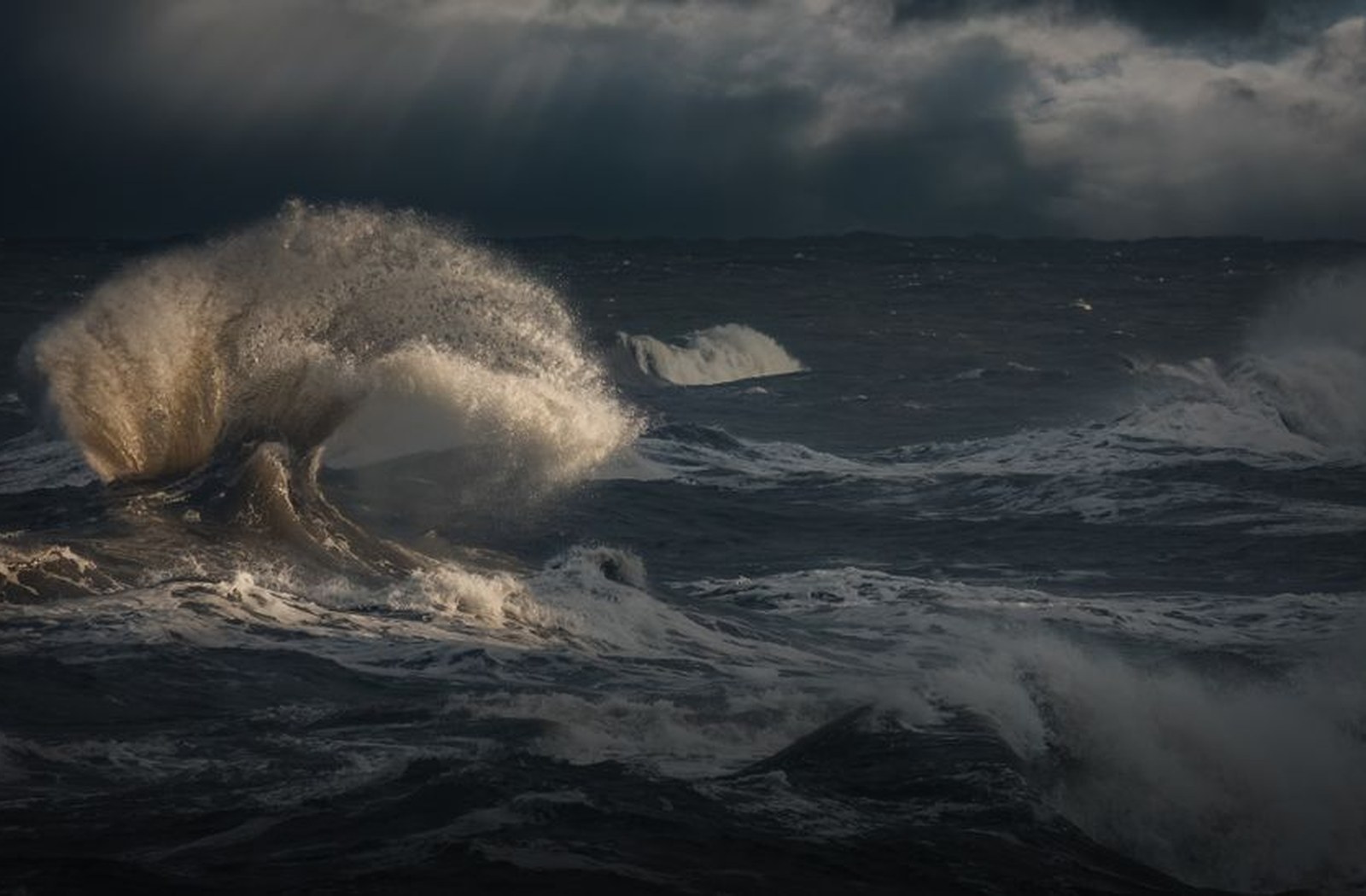 Dark sea and wind-driven waves under changing weather along a rocky shore.